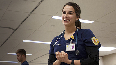 Female student dressed in scrubs talks to patient