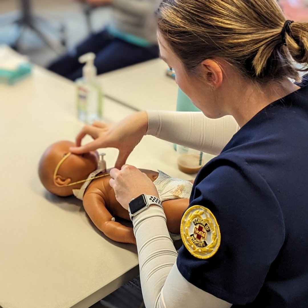Nursing student adjusts nasal cannula on an infant mannequin on a table.