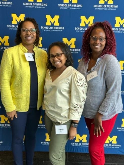 Three alumni proudly posing in front of a School of Nursing backdrop at an event.